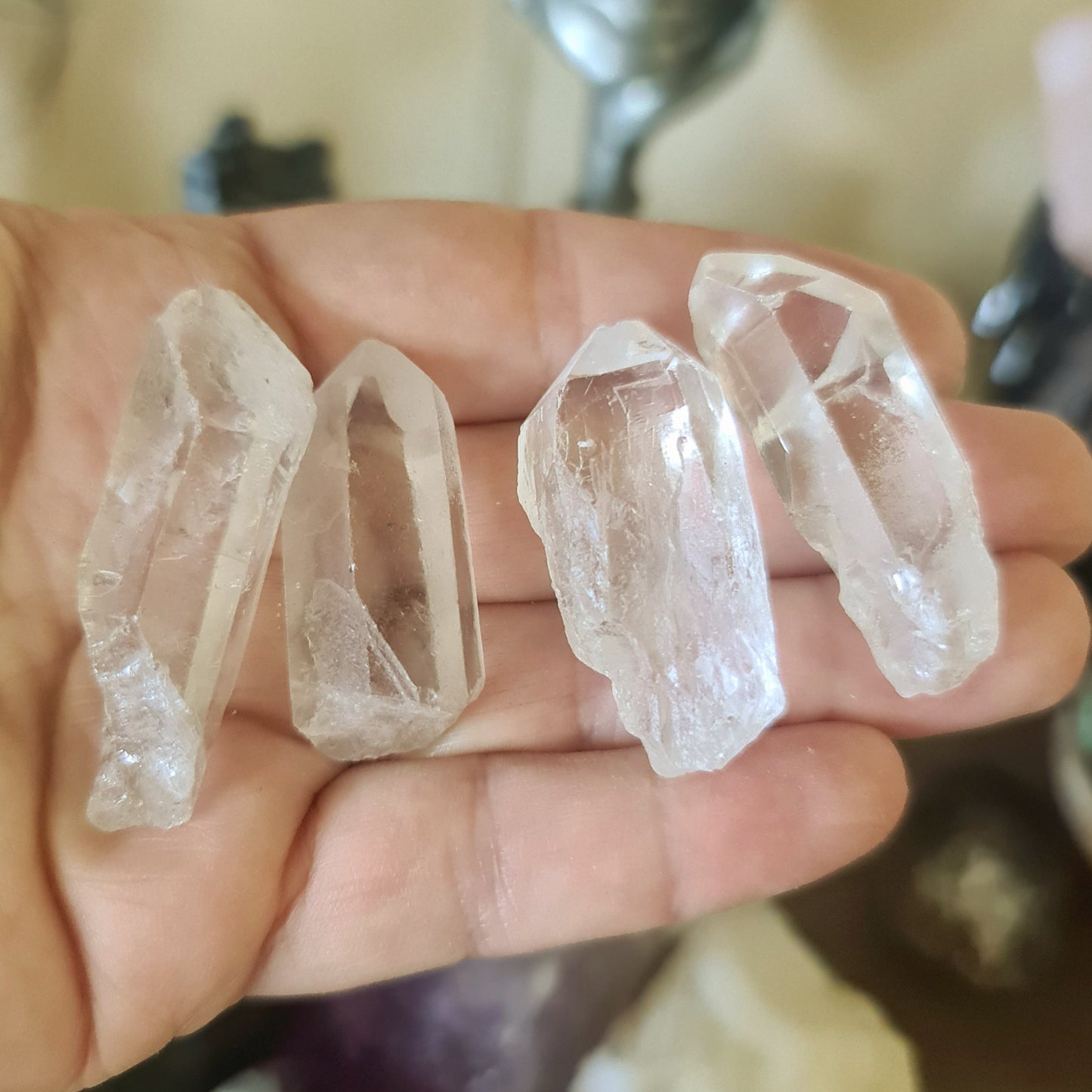A hand holding three clear quartz crystal points with a reflective, smooth surface.