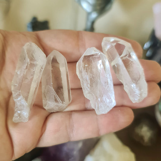 A hand holding three clear quartz crystal points with a reflective, smooth surface.