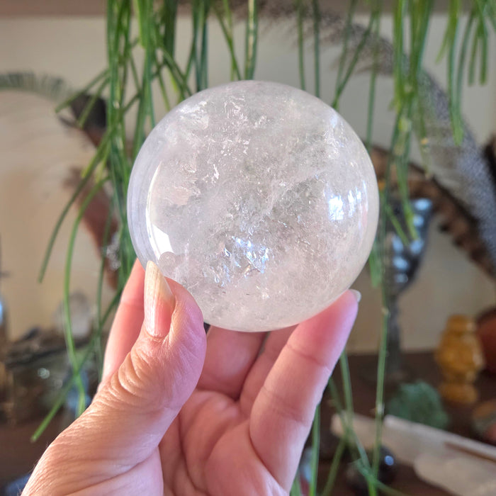 Clear crystal sphere held in a hand with a blurred indoor background