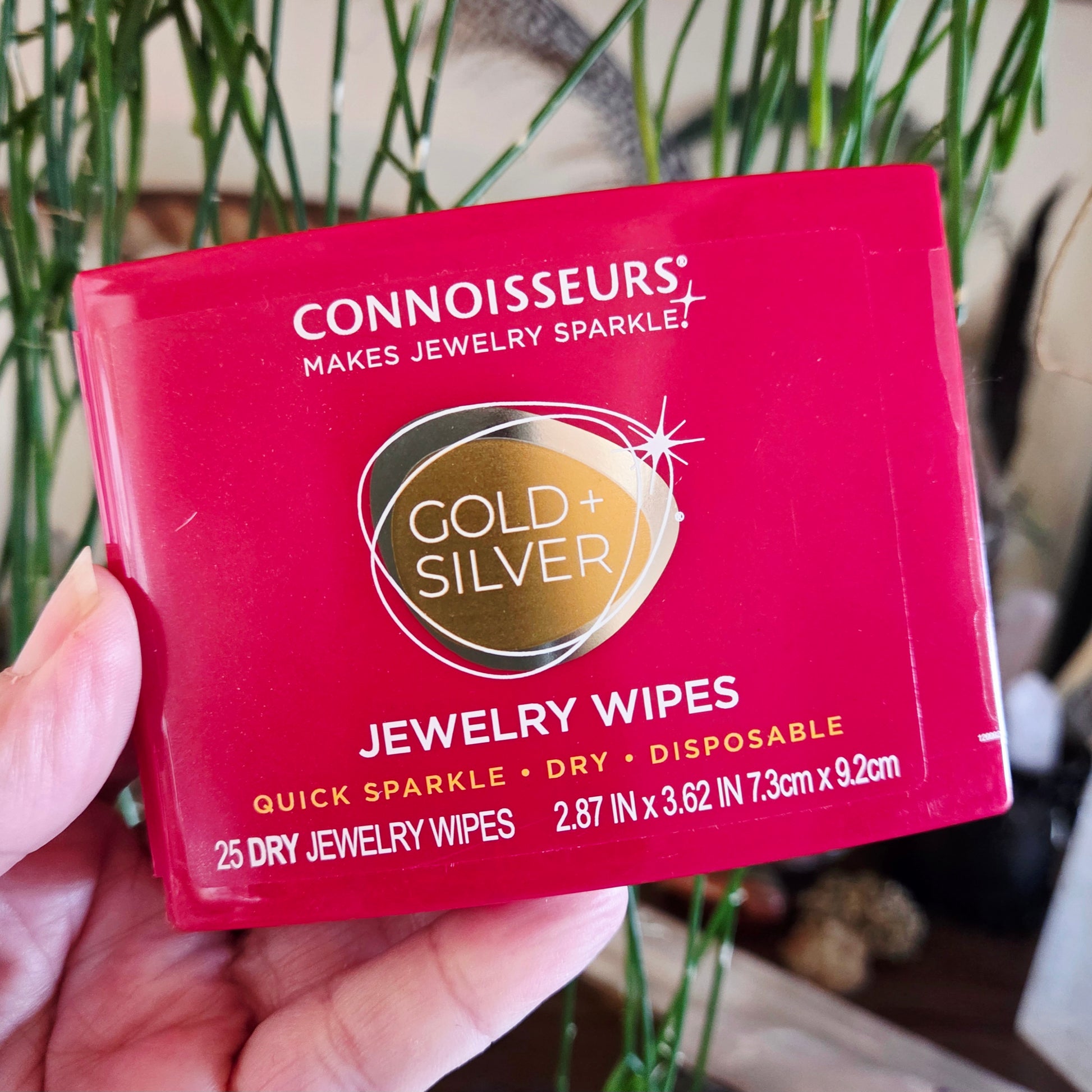 Connoisseurs Gold + Silver Jewelry Wipes packaging held in a hand with a blurred background