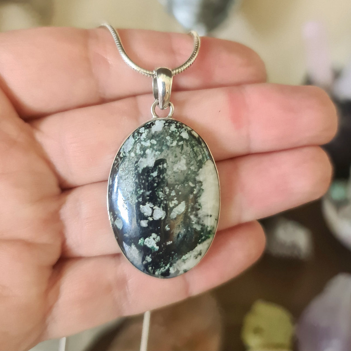 A sterling silver pendant with a marbled green and black stone, held in a person's hand.