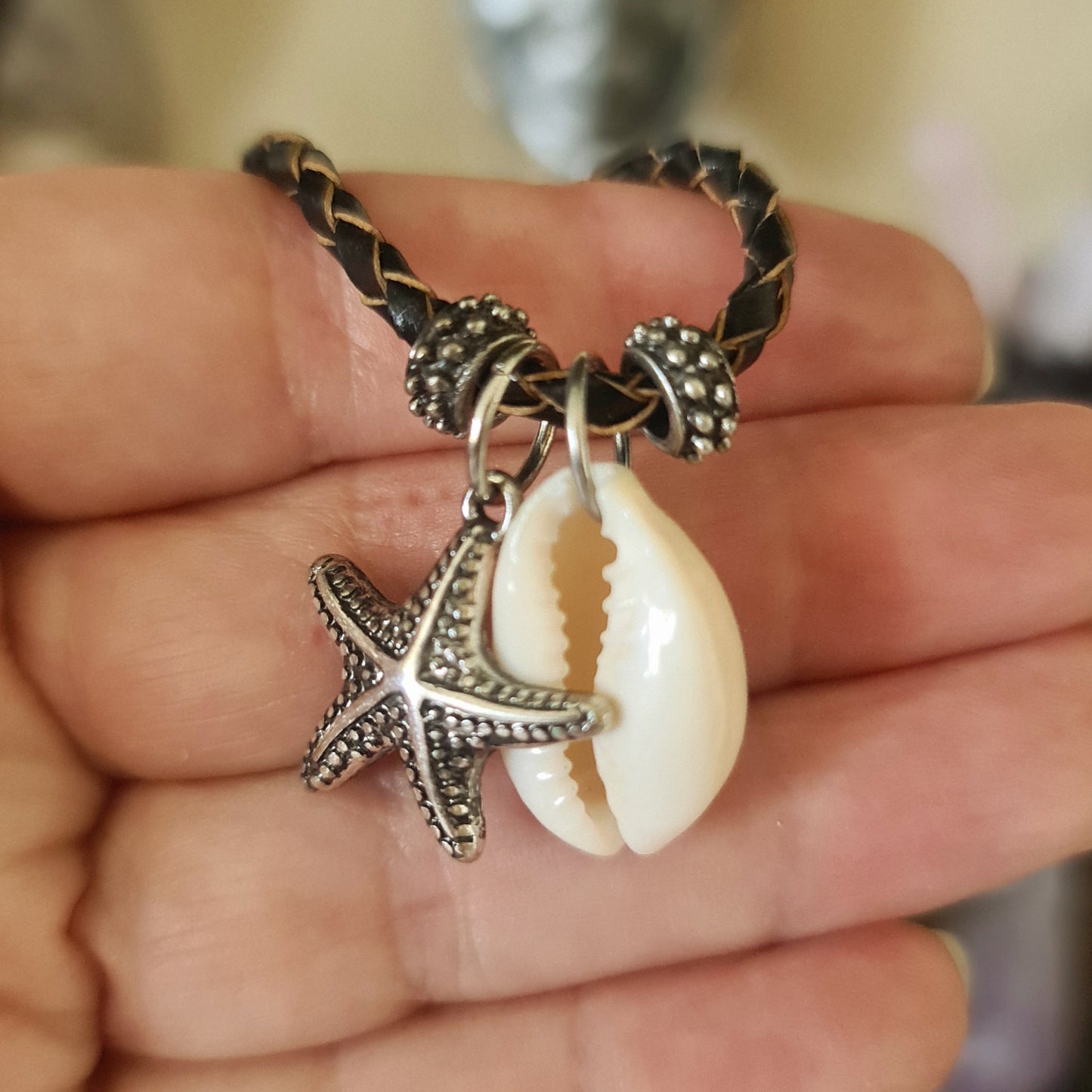 A cowrie starfish necklace with a silver finish on a leather necklace strap.