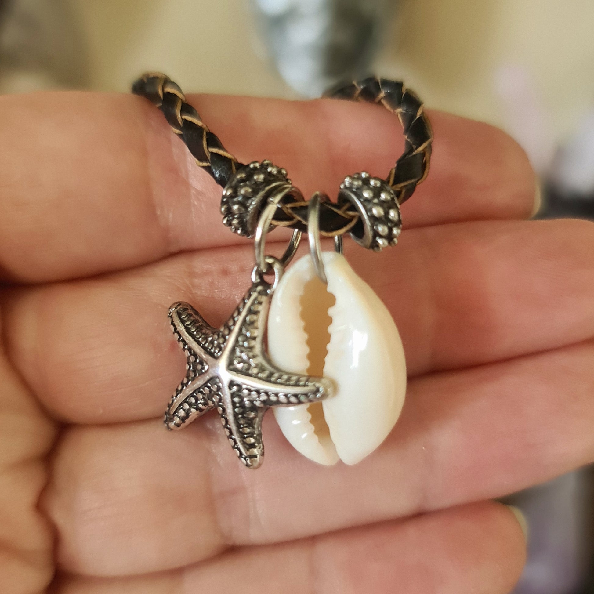 A cowrie starfish necklace with a silver finish on a leather necklace strap.