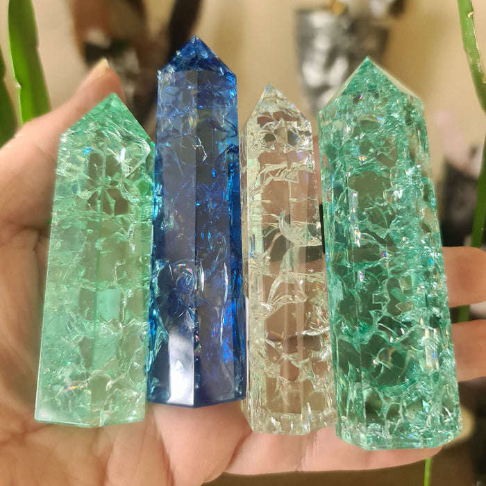 Three polished crackle quartz points in blue, green, and clear colors, held in a person's hand.