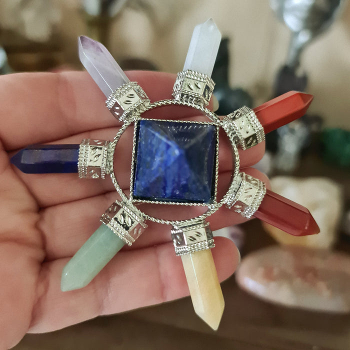 A hand holding a multicolored crystal chakra wheel with seven different colored crystals and a central crystal pyramid.