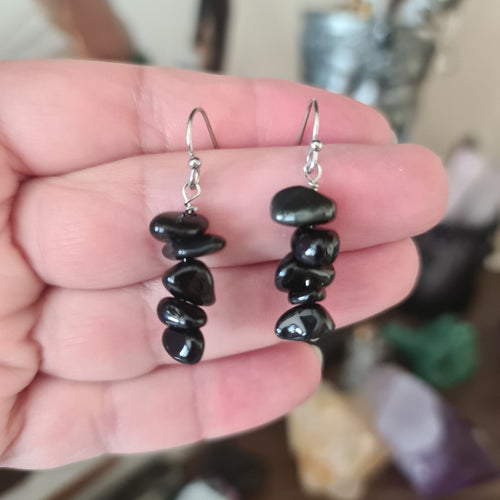 A pair of black obsidian stone chip earrings held in a person's hand, with silver plated ear wires.