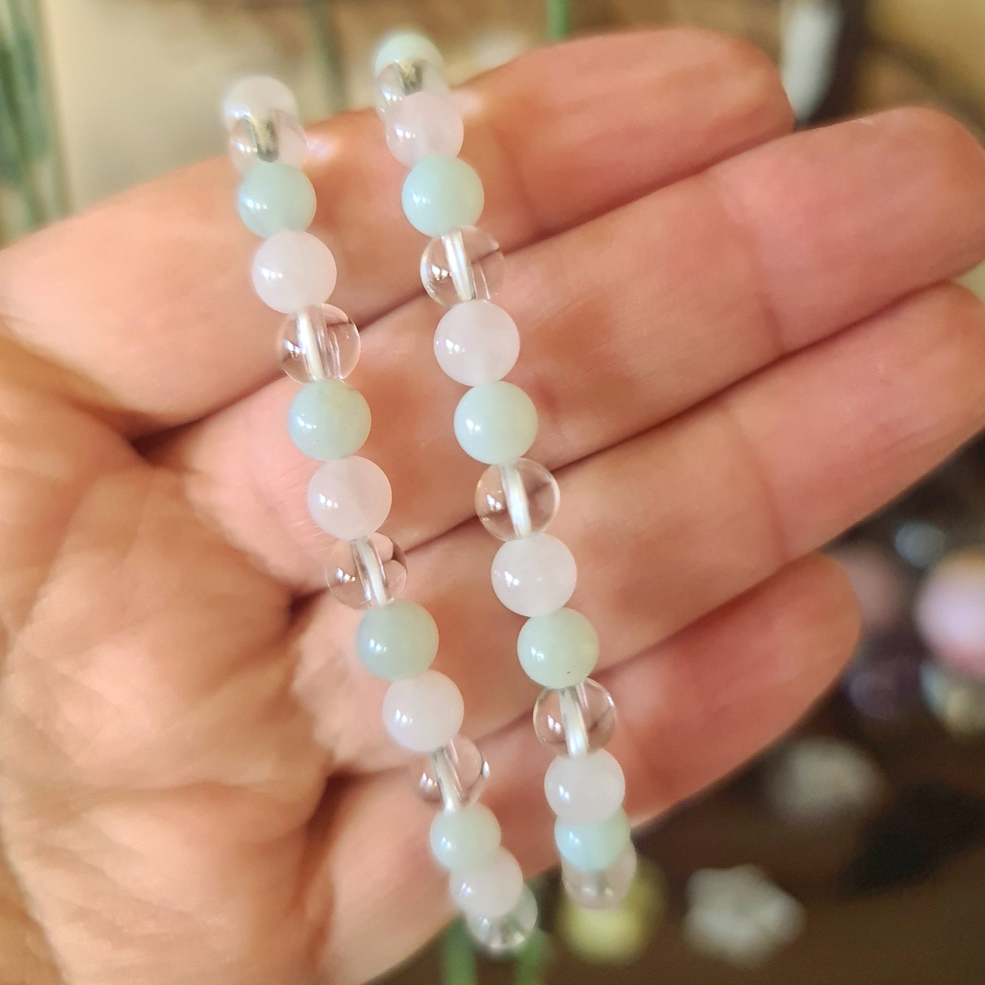 A hand holding a delicate beaded bracelet with a mix of clear, jade, and rose quartz crystals.