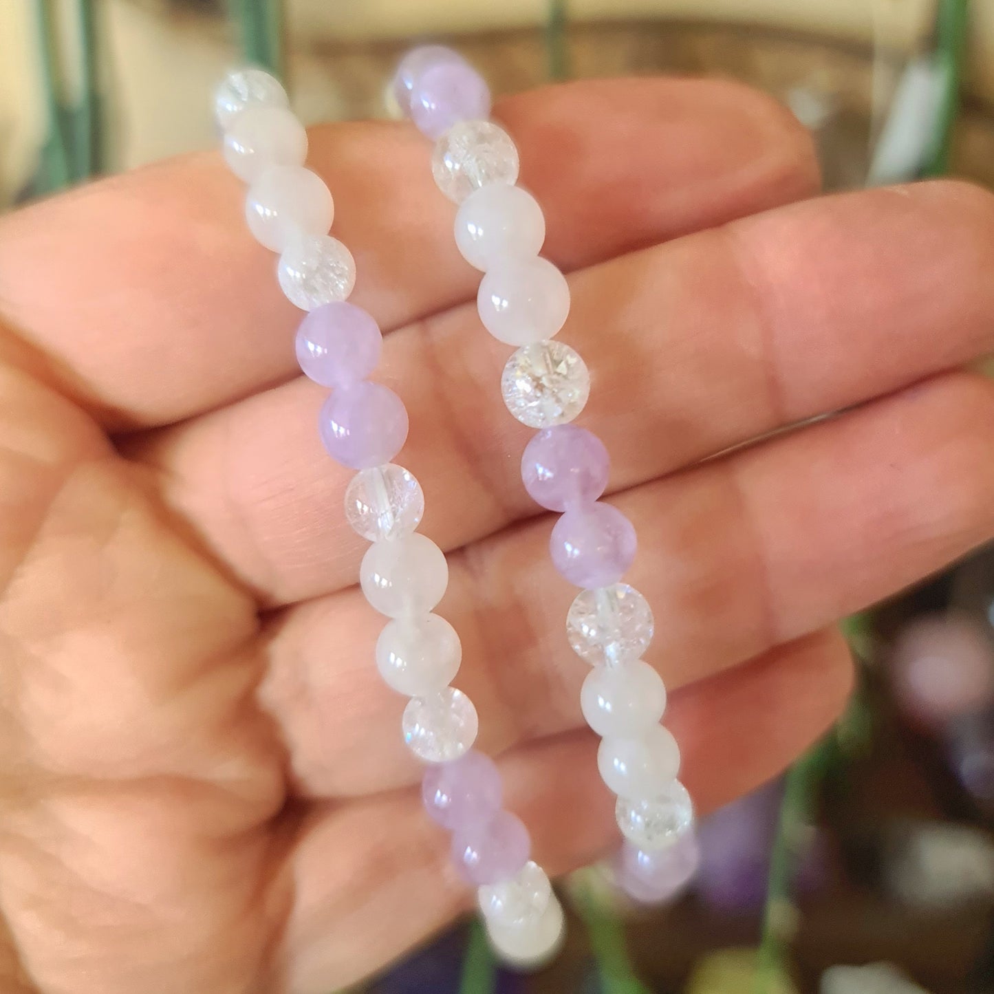 A hand holding two beaded bracelets with a combination of purple, clear, and rose quartz crystals.