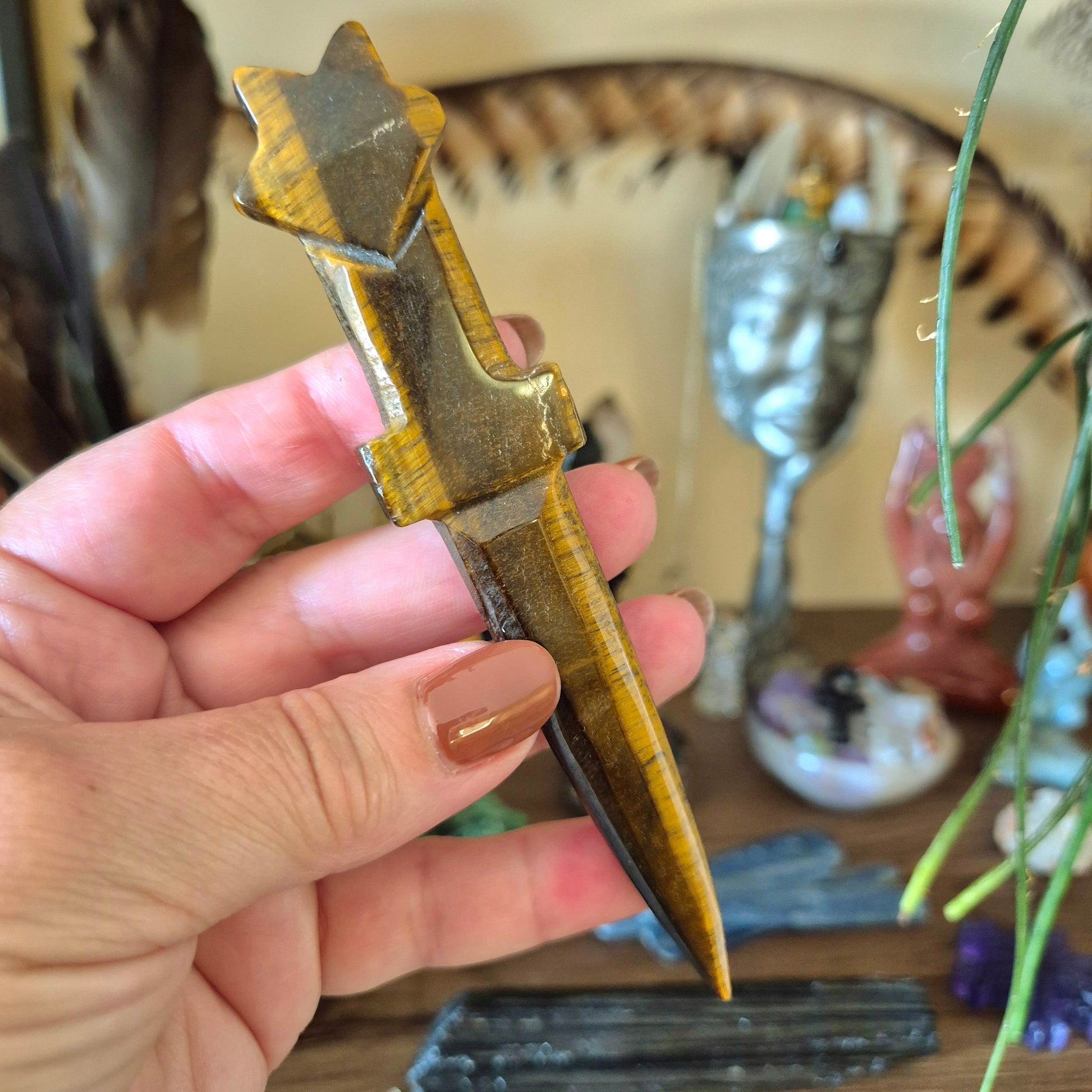 A hand holding a collectible dagger with a crystal-like handle and a metallic blade, against a backdrop of various collectible items.