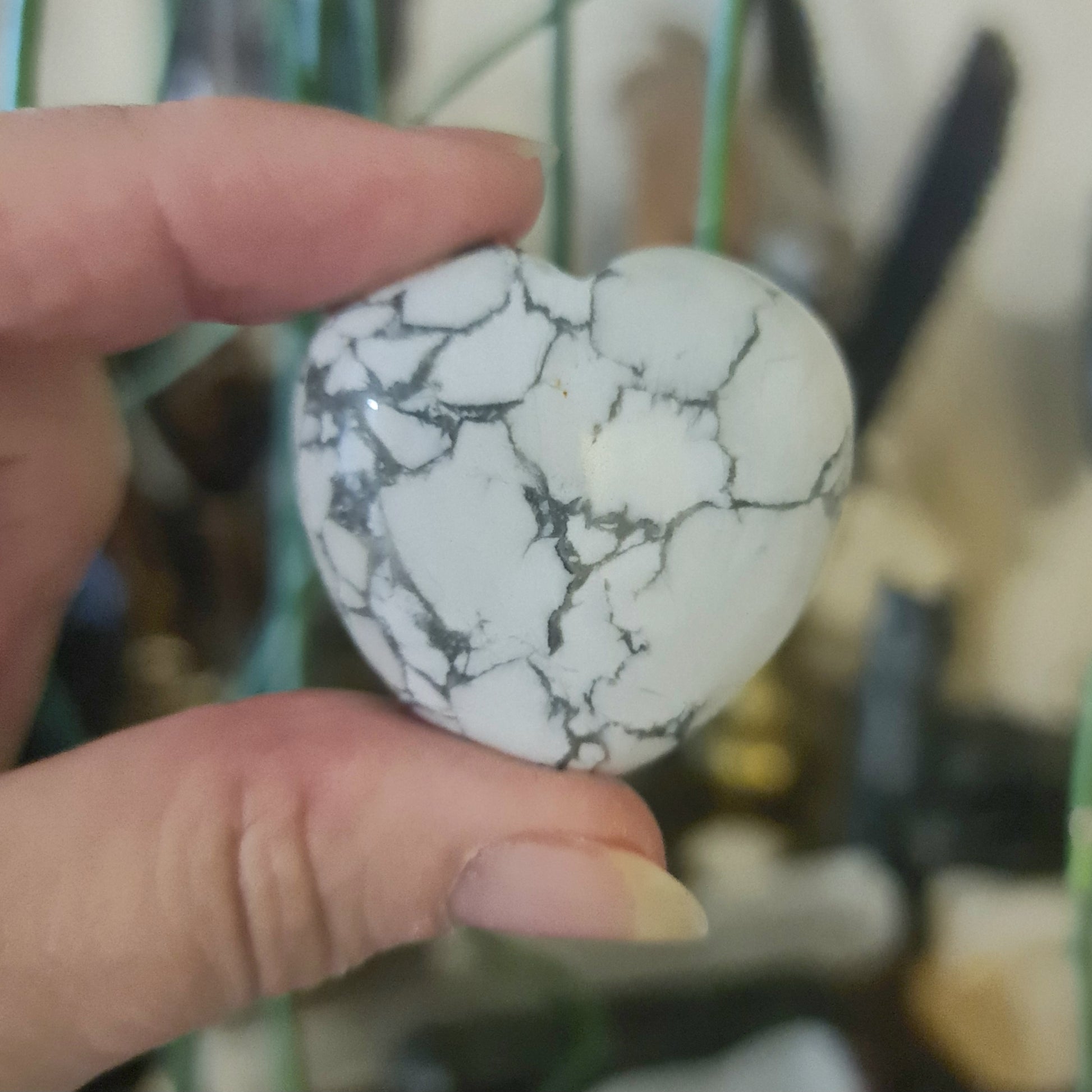 A hand holding a polished, heart-shaped crystal with a white and grey marble-like pattern.