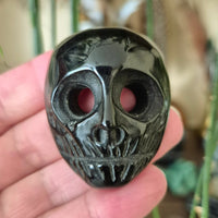 A close-up image of a black crystal mask with human-like features, held in a person's hand.