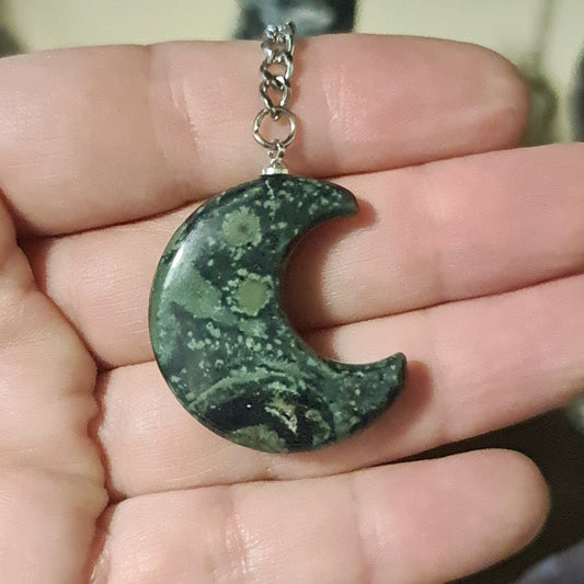 A hand holding a keyring with a green crystal moon charm.