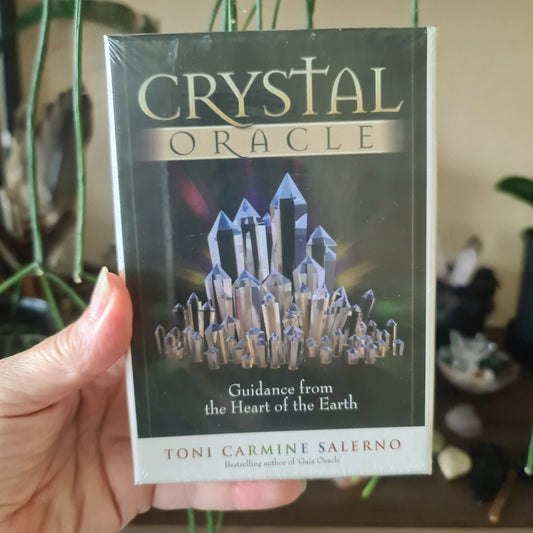 A hand holding a pack of 'Crystal Oracle' cards with a visual of crystals on the cover.