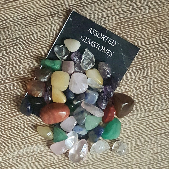 Assorted colorful gemstone chips and small tumbles displayed in front of a black card with the text 'Assorted Gemstones'.