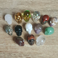 A collection of small crystal skulls in various colors and designs, displayed on a wooden surface.