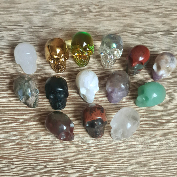 A collection of small crystal skulls in various colors and designs, displayed on a wooden surface.
