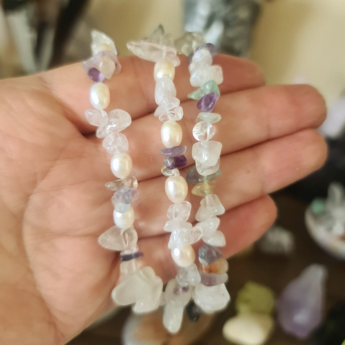 A hand holding a multicolored beaded bracelet with a mix of fluorite and clear quartz gems.