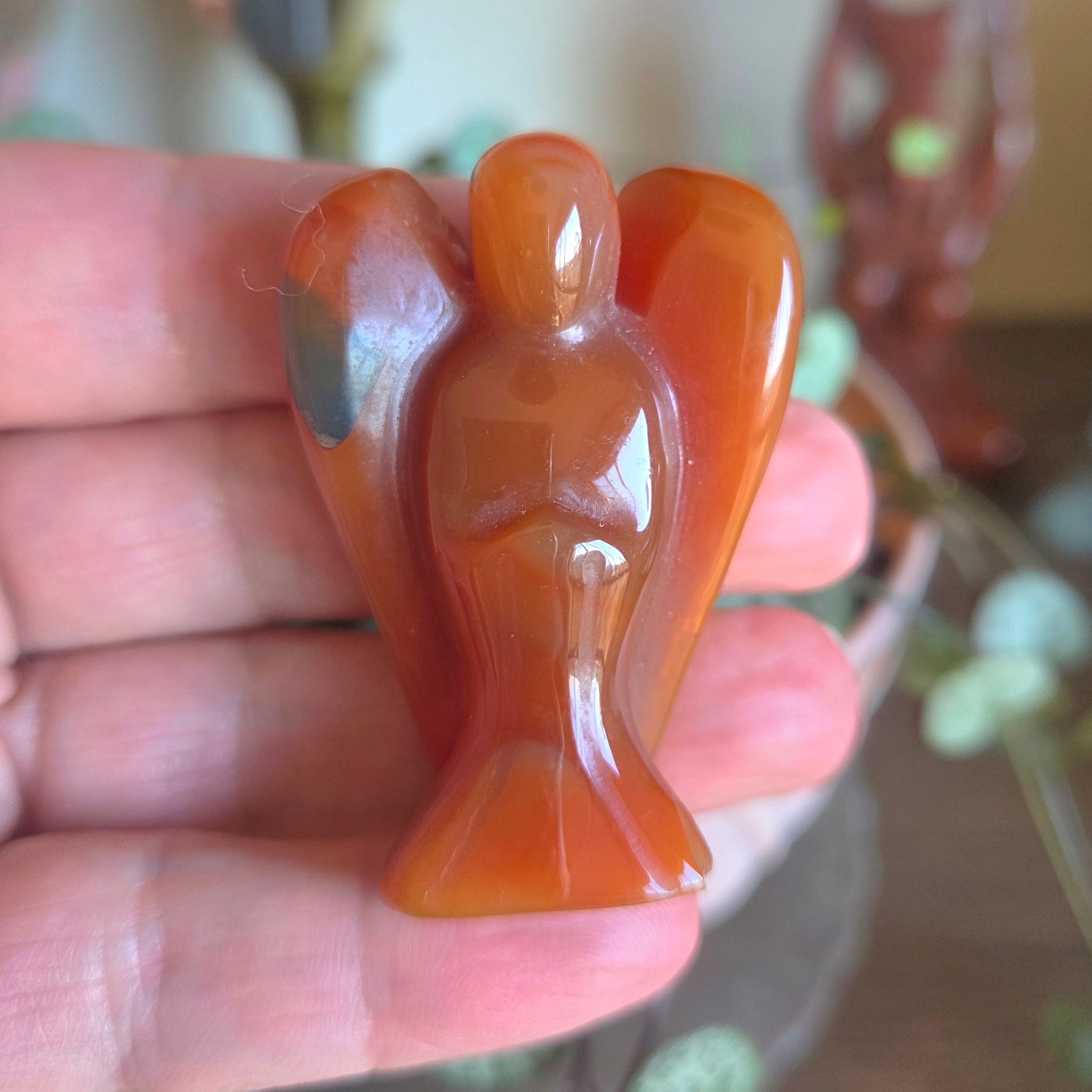 A small glossy angel-shaped carved stone or resin figurine held in a person's hand, with a softly blurred indoor background.