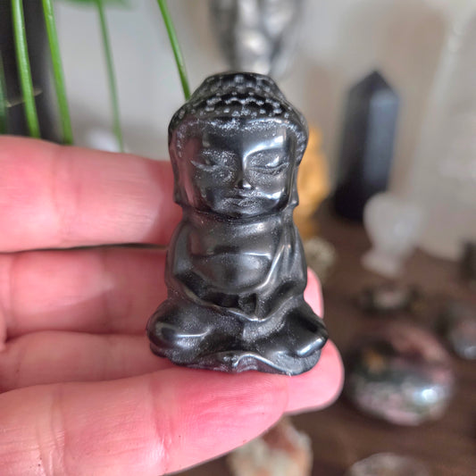 Small black Buddha figurine held in a hand with a blurred background