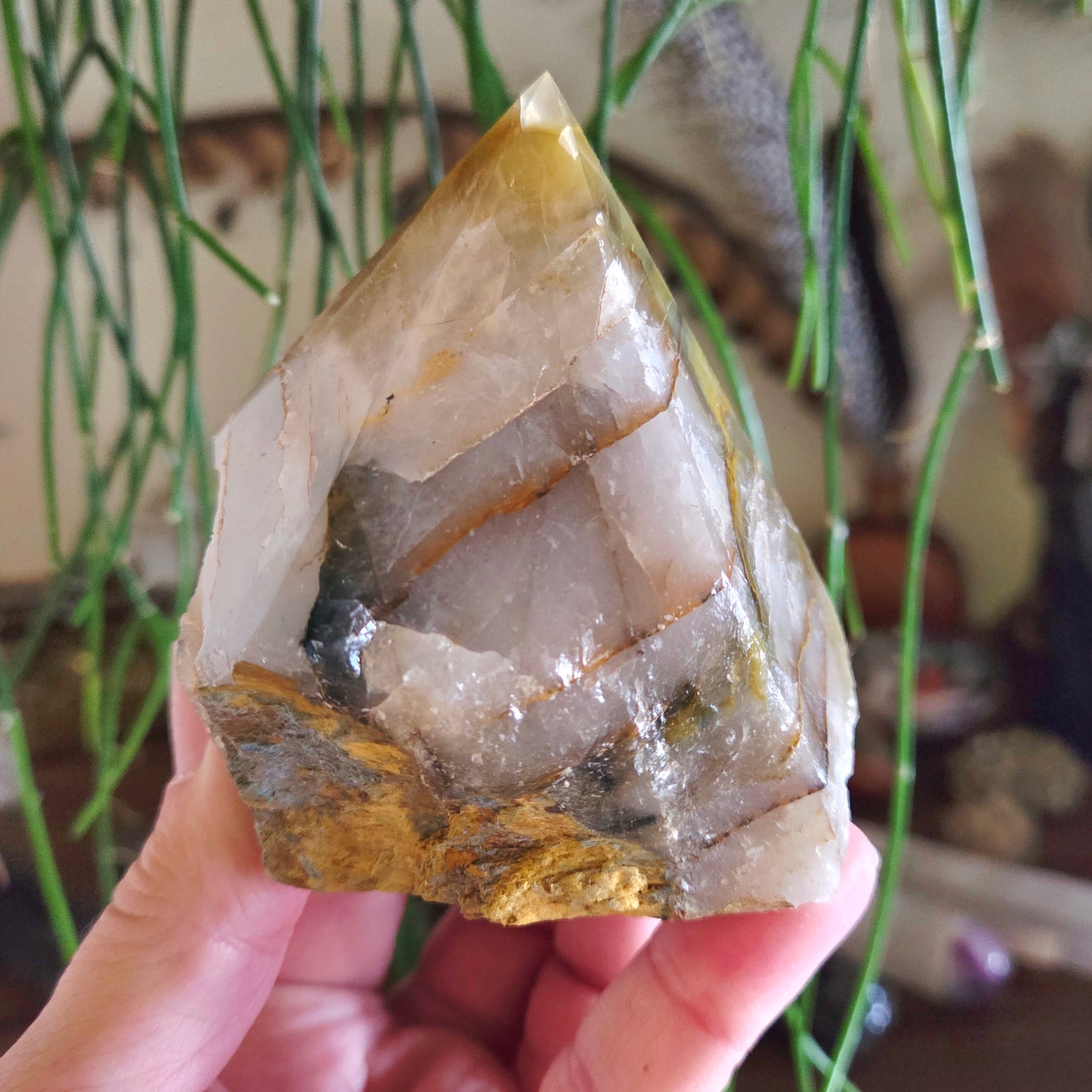 A polished stone point held in a hand, with visible crystal inclusions and a yellowish tint.