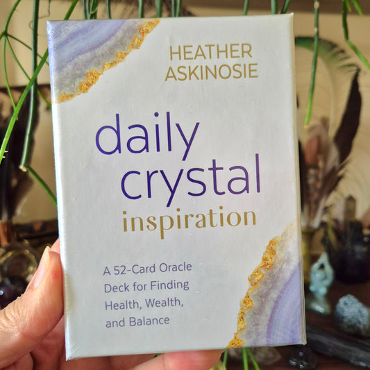 A hand holding a pack of 'Daily Crystal Inspiration' cards with a blue and gold cover design.