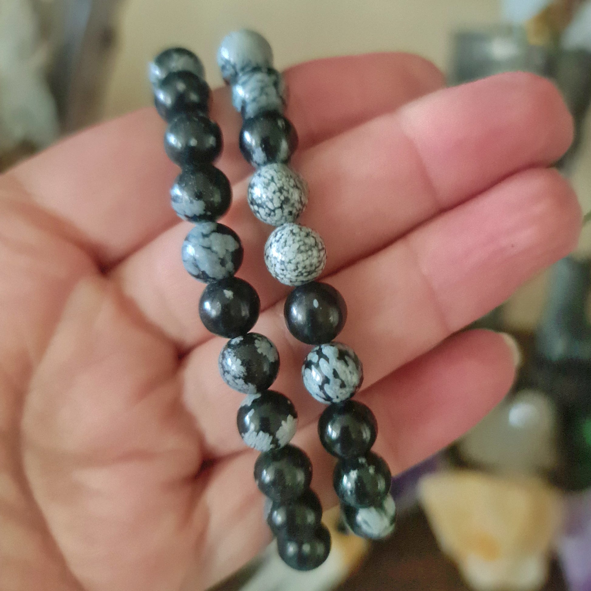 A hand holding two black and gray Dalmatian jasper stones with a marbled pattern, indicating they are polished and smoothed for use as a bracelet.