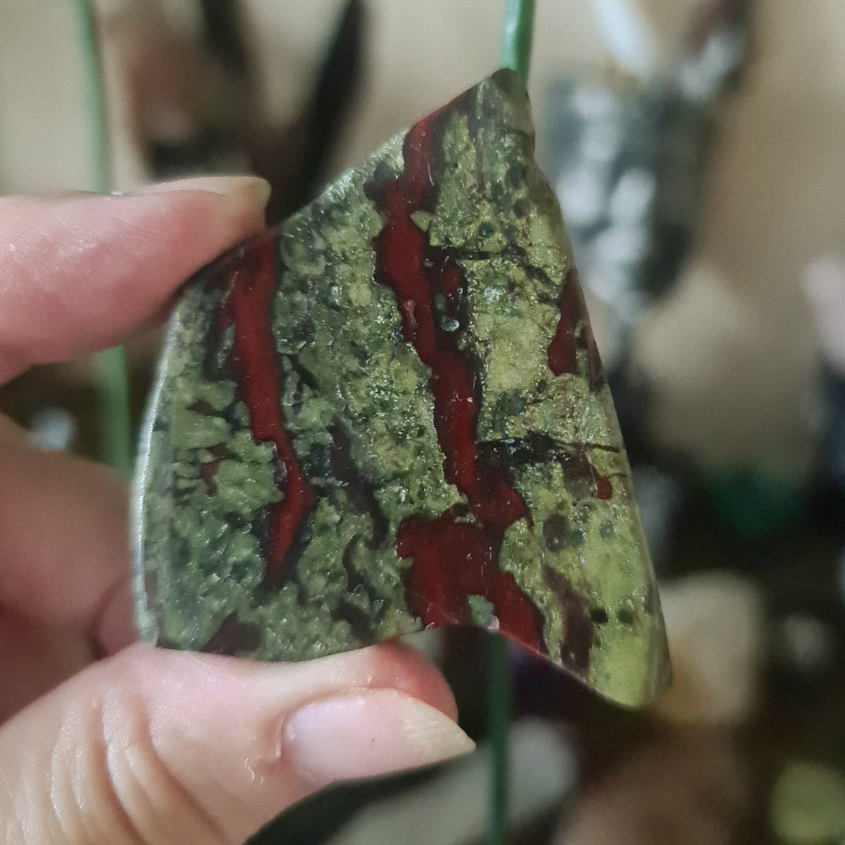 A hand holding a polished slab of red and green Dragon Stone with a crystalline pattern.