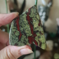 A hand holding a polished slab of red and green Dragon Stone with a crystalline pattern.