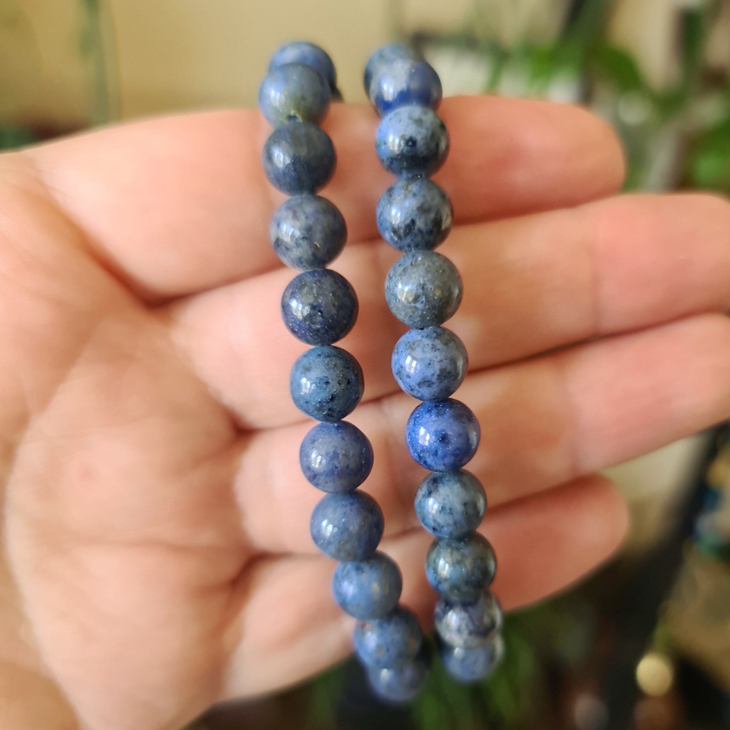 A hand holding a series of blue Dumortierite beads, typically used for making bracelets.