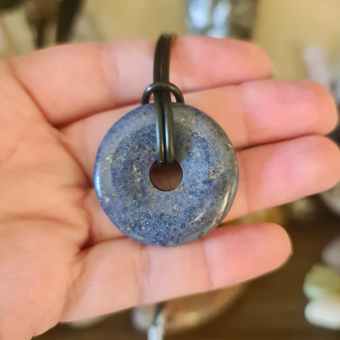 A blue donut-shaped crystal pendant on a black leather cord necklace.