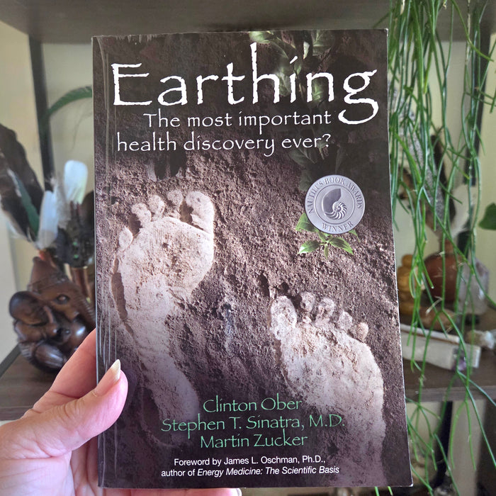 Book titled 'Earthing' held by a person with plants in the background