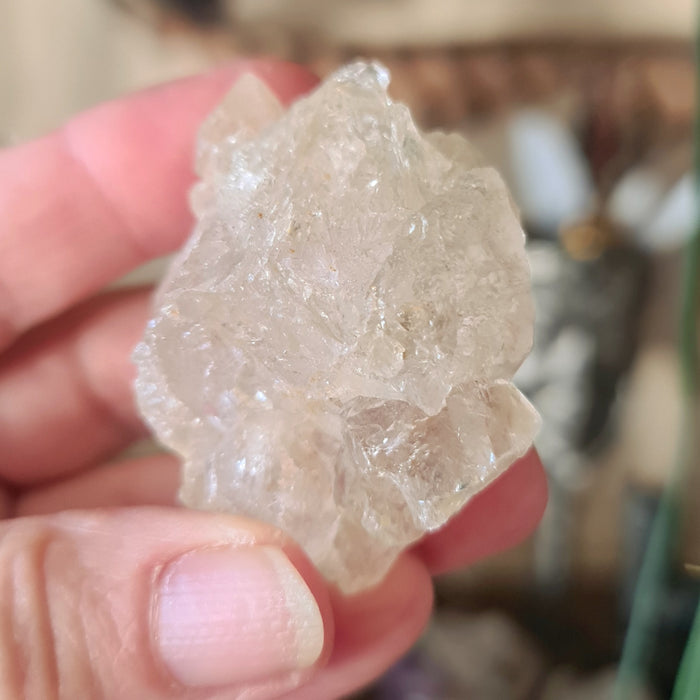 A hand holding a clear, rough-shaped quartz crystal.