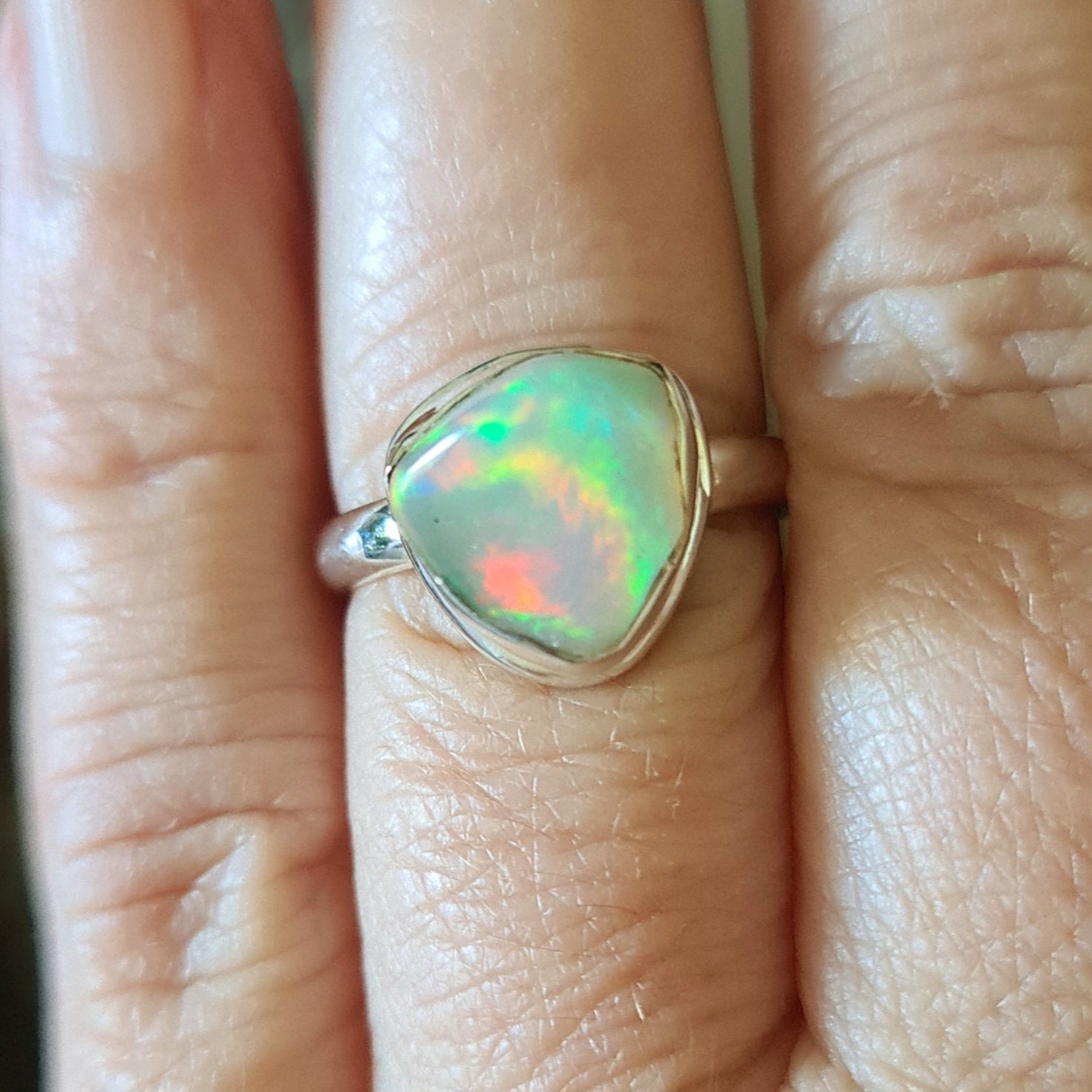A person's hand displaying a sterling silver ring with a multicolored opal stone.