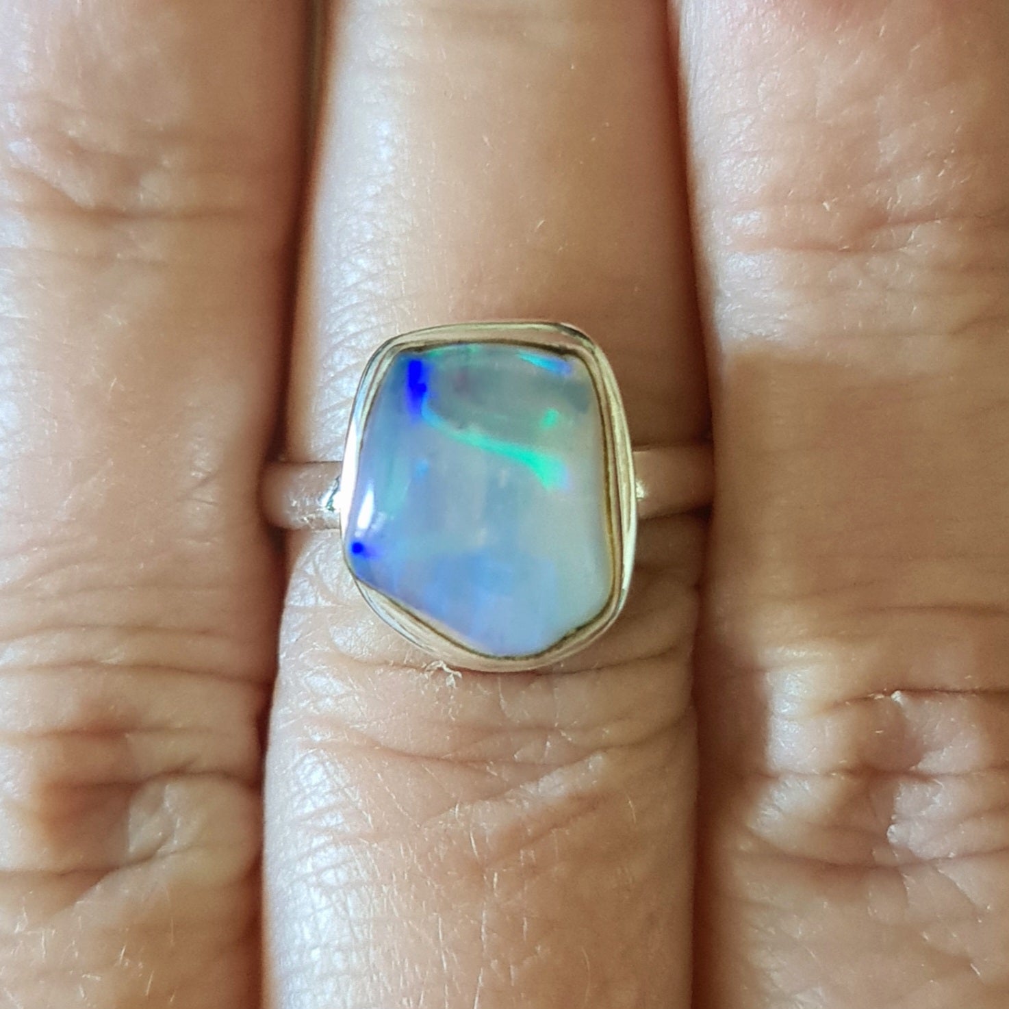 A hand displaying a sterling silver Ethiopian opal ring with a blue and green opal centerpiece.