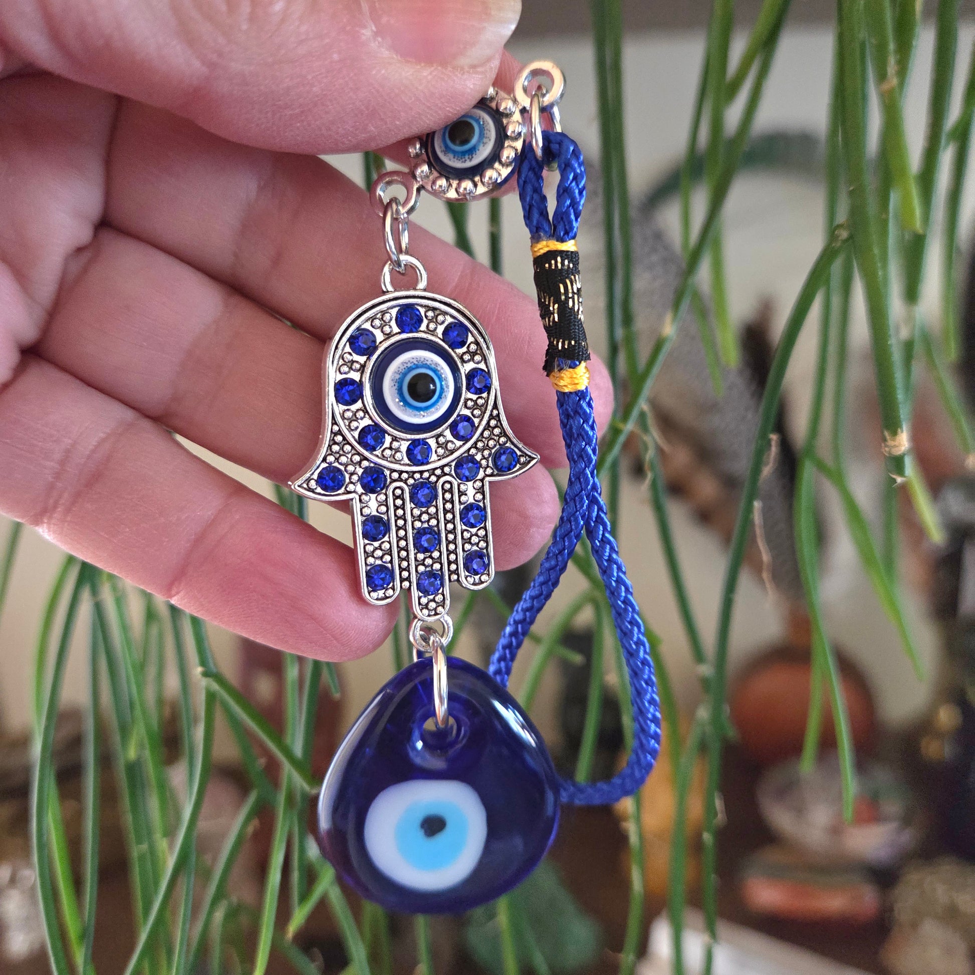 Hand holding a blue evil eye charm with hamsa hand design against a blurred background
