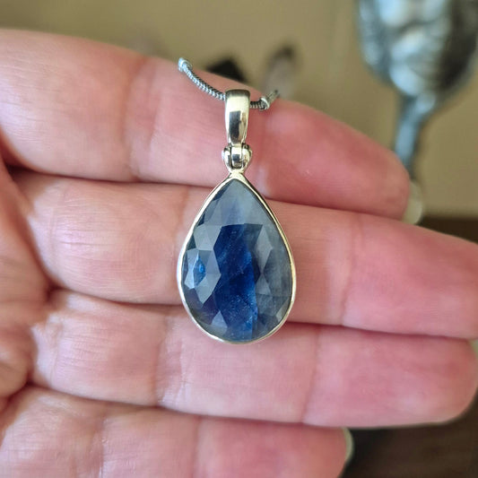 A faceted sapphire pendant necklace held in a person's hand, with a silver-colored metal chain.