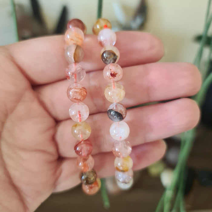 A hand holding a Fire Quartz bracelet with multicolored stones.