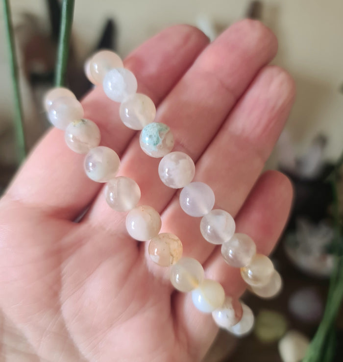 A hand holding a Flower Agate bracelet with multiple translucent stones on a chain.