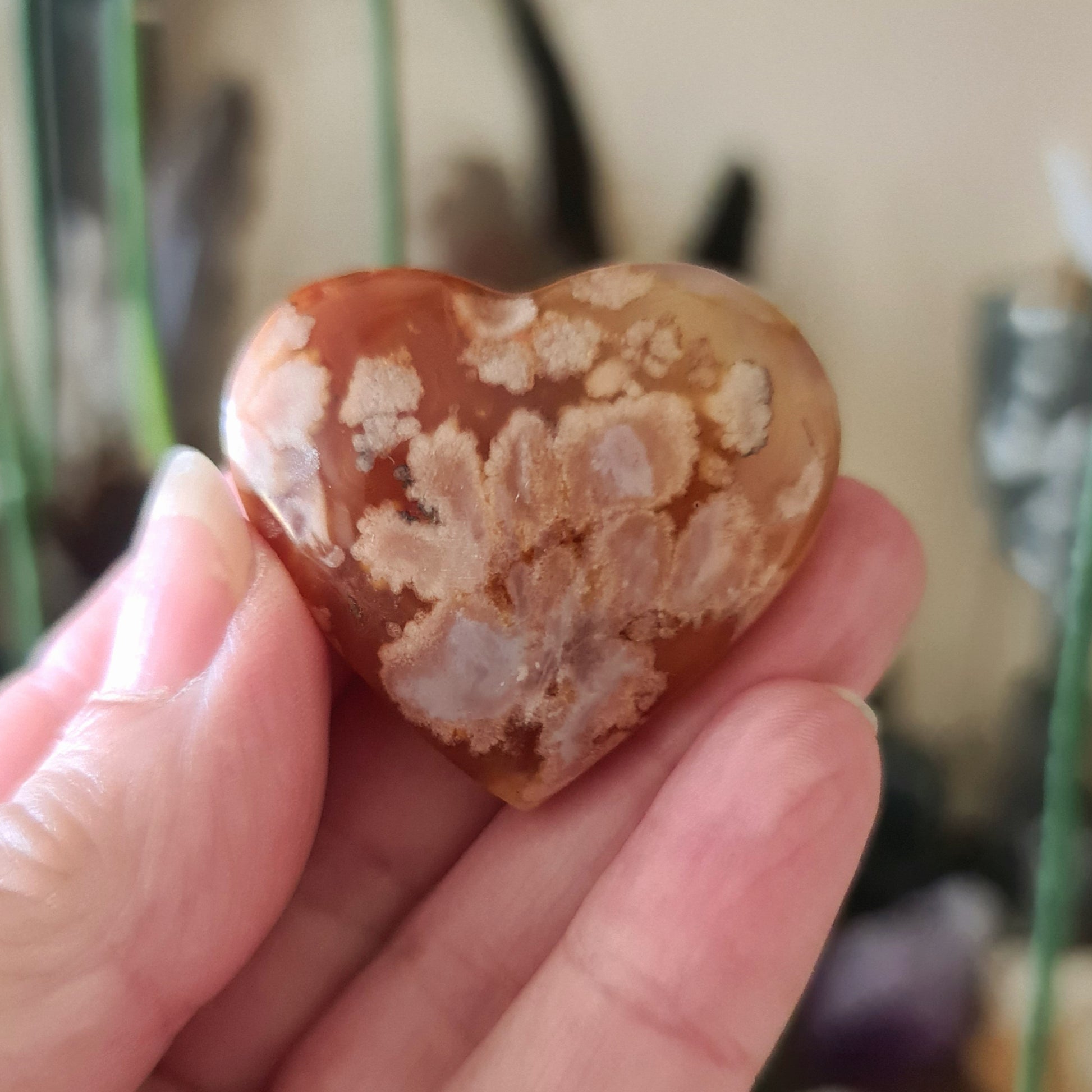 A small heart-shaped Flower Agate crystal being held in a person's hand.