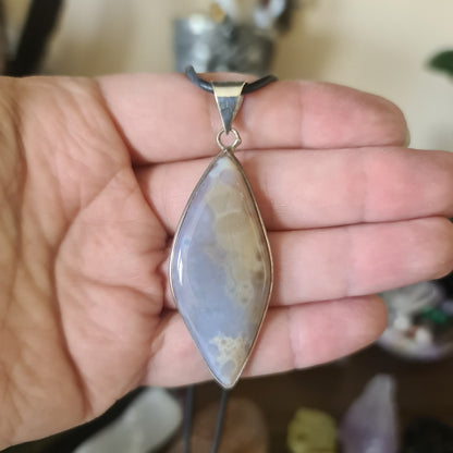 A teardrop-shaped Flower Agate pendant with a metallic silver setting, held in a hand.