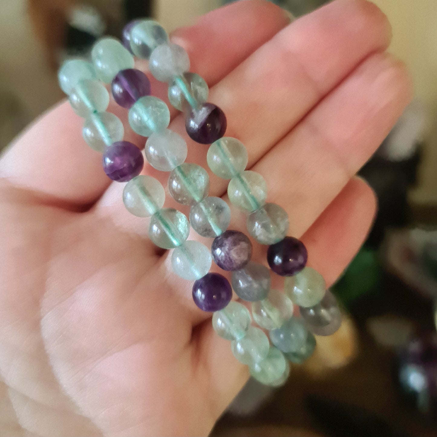 A hand holding a fluorite bracelet with a mix of purple, green, and clear colored beads.
