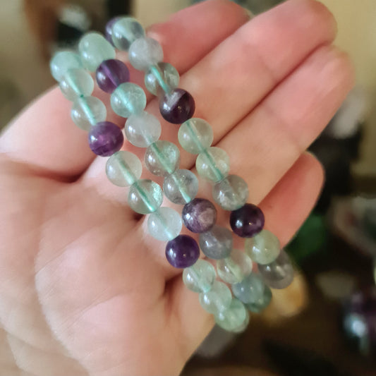 A hand holding a fluorite bracelet with a mix of purple, green, and clear colored beads.