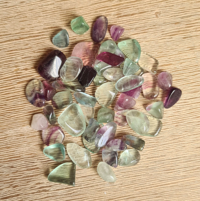 A collection of various colored fluorite chip tumbles arranged on a wooden surface.
