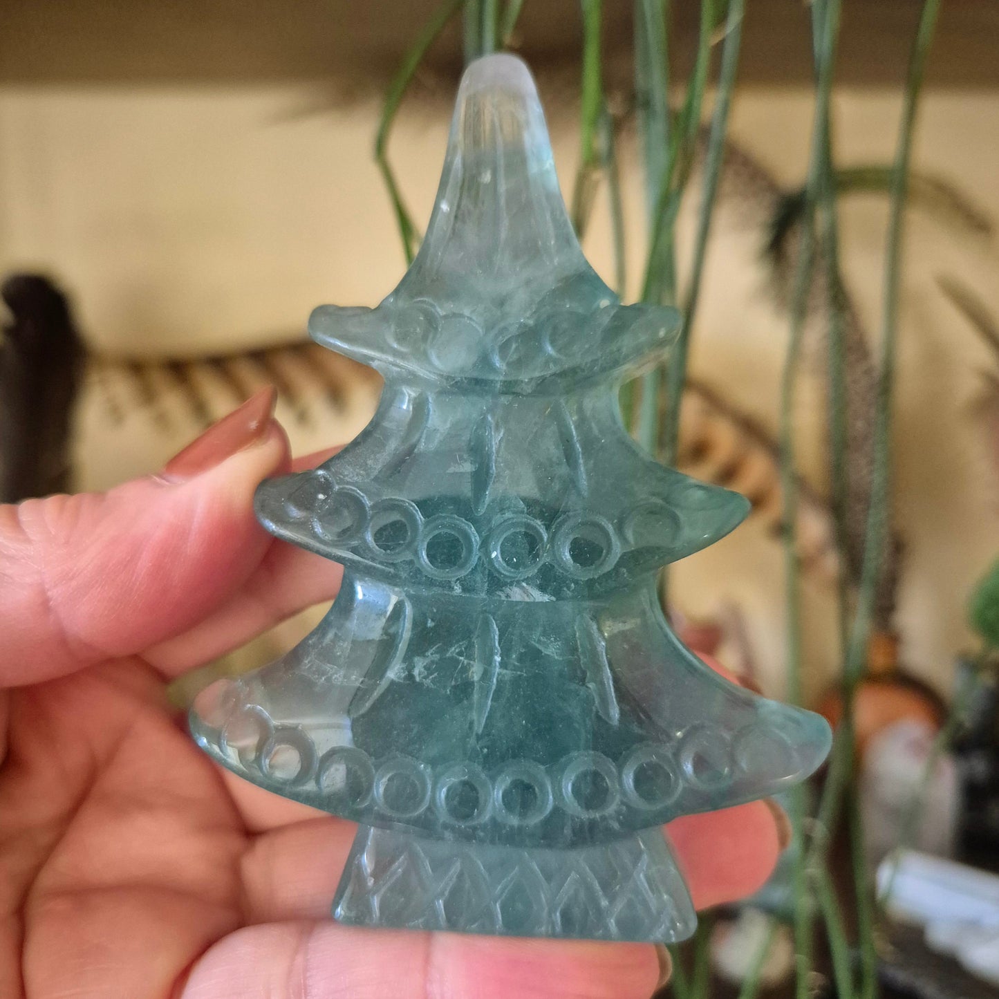 A hand holding a fluorite crystal shaped like a Christmas tree, with a milky green color and multiple holes on its surface.