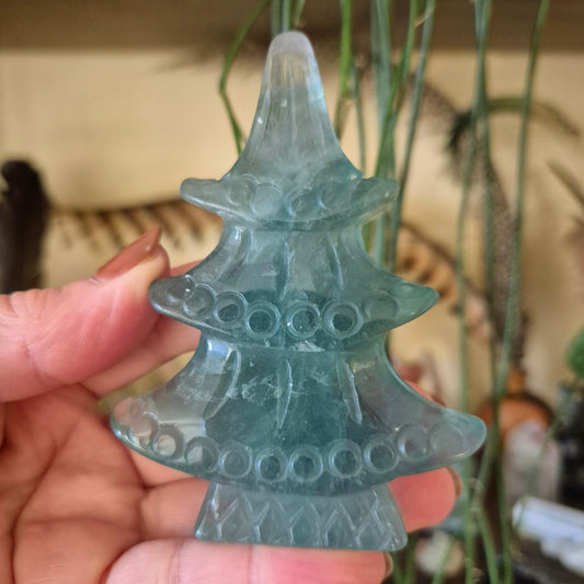 A hand holding a fluorite crystal shaped like a Christmas tree, with a milky green color and multiple holes on its surface.