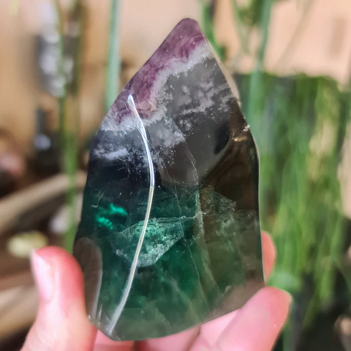 A polished green fluorite crystal with a metallic sheen, held in a person's hand.