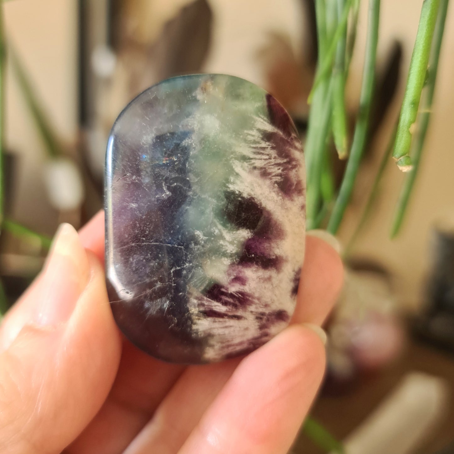 A polished Fluorite tumbled stone held in a person's hand, with a green and purple color pattern.