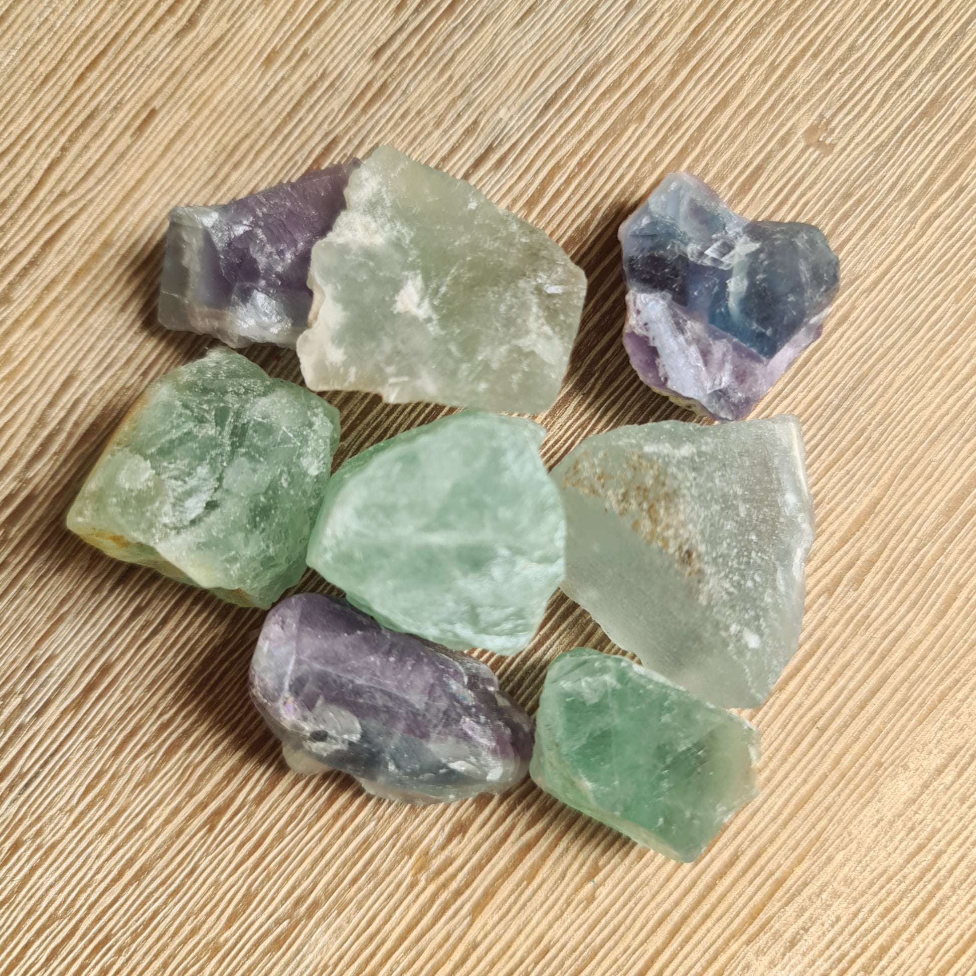 A collection of various colored Fluorite raw crystals placed on a wooden surface.