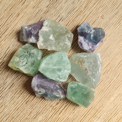 A collection of various colored Fluorite raw crystals placed on a wooden surface.