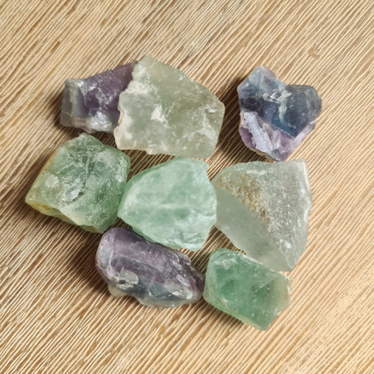 A collection of various colored Fluorite raw crystals placed on a wooden surface.
